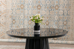 A round black table with a glossy finish is centered in the image. Atop the table is a black vase with a white stripe holding a bouquet of white tulips. The background features an intricately patterned, blue and beige Tabriz Rug, North West Persia, 11' x 14' from Ben Soleimani.