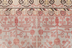 A close-up of an intricately woven heirloom-quality rug with a detailed pattern. The design features geometric shapes, floral motifs, and symmetrical arrangements in shades of red, pink, grey, and beige. The rug's slightly worn texture suggests it is **Ben Soleimani's KHOTAN RUG, AR30065 from East Turkestan**, measuring 5'11" x 11'1", that has been cherished over the years.