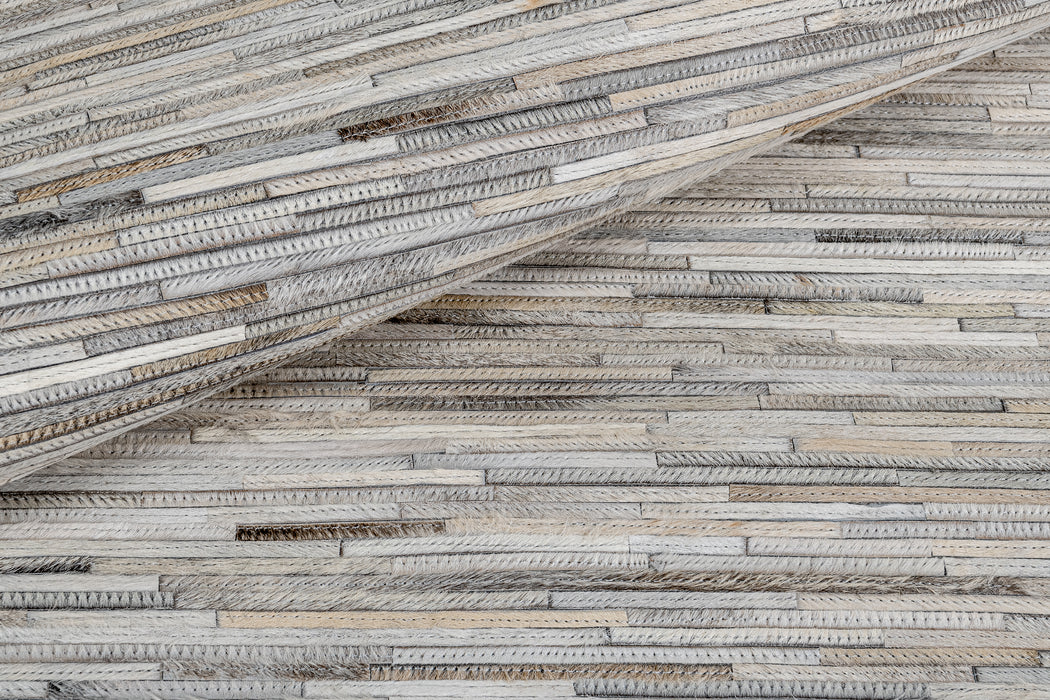 Close-up of a textured surface made of narrow wooden strips laid out in horizontal lines. The wood pieces vary slightly in color and length, creating a natural, slightly rustic pattern. One section of the surface is folded over another, reminiscent of the attention to detail found in the Ladro Hide – Grey by Ben Soleimani collection.